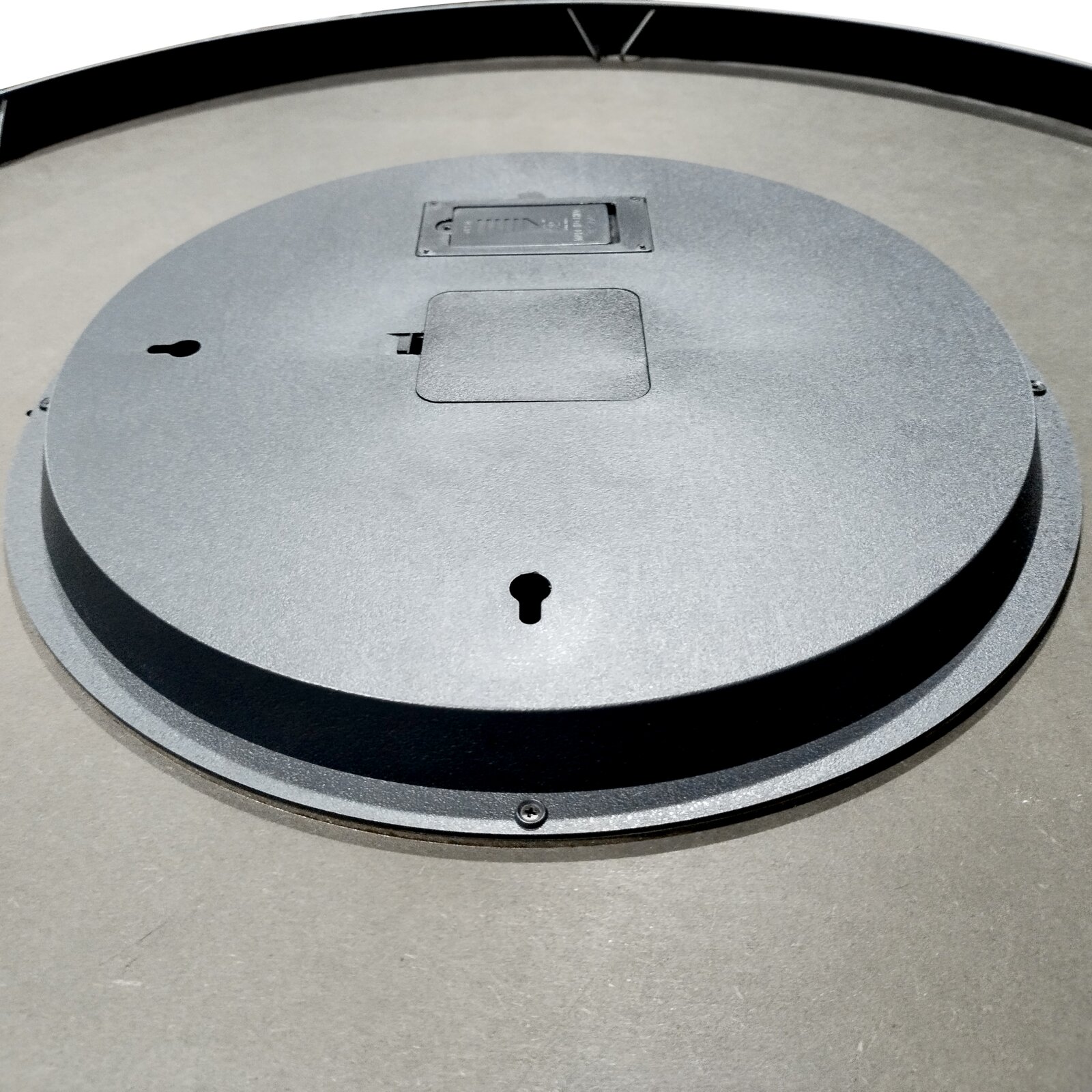 Achterkant van een ronde wandspiegel met zwarte lijst en metalen ophanging, schuin van bovenaf gefotografeerd
