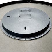 Achterkant van een ronde wandspiegel met zwarte lijst en metalen ophanging, schuin van bovenaf gefotografeerd