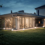 Moderne Terrasse mit Glasfront und beleuchteten Erdspießen in der Abenddämmerung, seitliche Perspektive