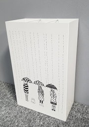 Weißer Papierkorb/Aufbewahrungsbehälter mit schwarz-weißer Regenschirm-Illustration und Regenlinien, schräg von vorne links fotografiert