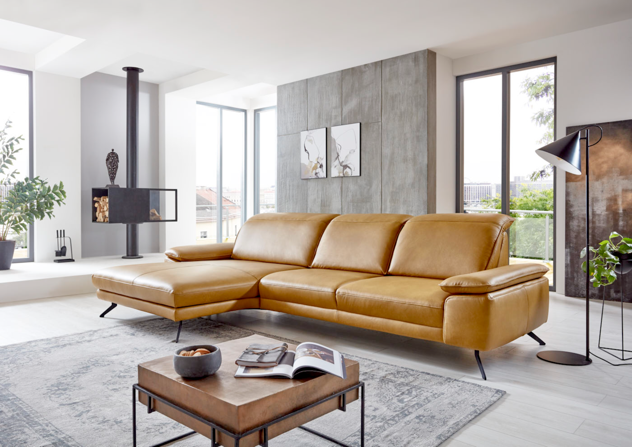 Moderne Longchairkombination in senffarbenem Leder, seitliche Perspektive in einem hellen Wohnzimmer mit großen Fenstern und stilvoller Dekoration.