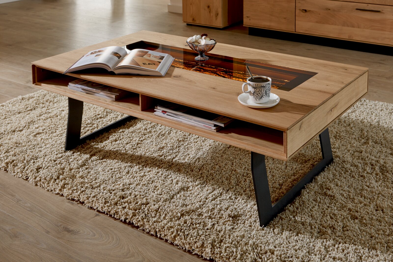Moderner Couchtisch aus Holz mit schwarzem Metallgestell, seitliche Perspektive, dekoriert mit einer Tasse Kaffee und einem Buch auf einem Teppich.