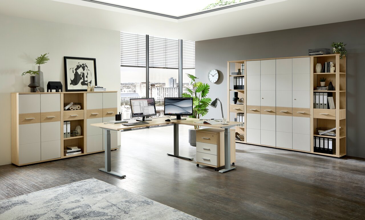 Moderne Büroumgebung mit einem Winkelschreibtisch, zwei Monitoren, einem Rollcontainer und mehreren Aktenschränken und Regalen in Holzoptik. Perspektive: Frontalansicht des Schreibtischs und der Schränke.