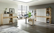 Moderne Büroumgebung mit einem Winkelschreibtisch, zwei Monitoren, einem Rollcontainer und mehreren Aktenschränken und Regalen in Holzoptik. Perspektive: Frontalansicht des Schreibtischs und der Schränke.