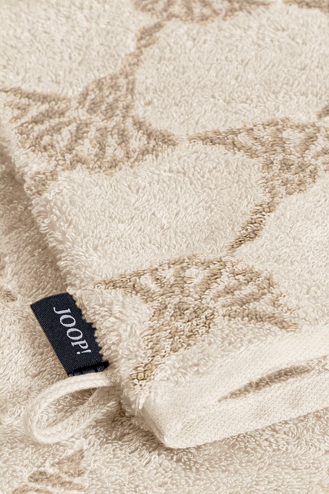 JOOP! Waschhandschuh Nahaufnahme eines beigen Waschhandschuhs mit dezentem Muster und einer schwarzen Joop!-Markenlasche.