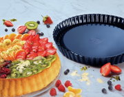 Obstkuchenform 28 cm BackLiebe, schwarze runde Backform neben einem dekorierten Obstkuchen, Draufsicht.