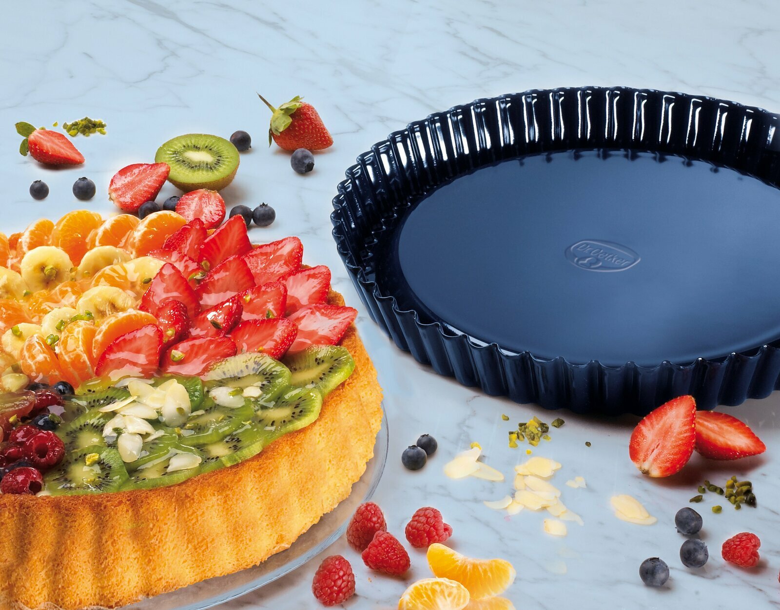 Obstkuchenform 28 cm BackLiebe, schwarze runde Backform neben einem dekorierten Obstkuchen, Draufsicht.