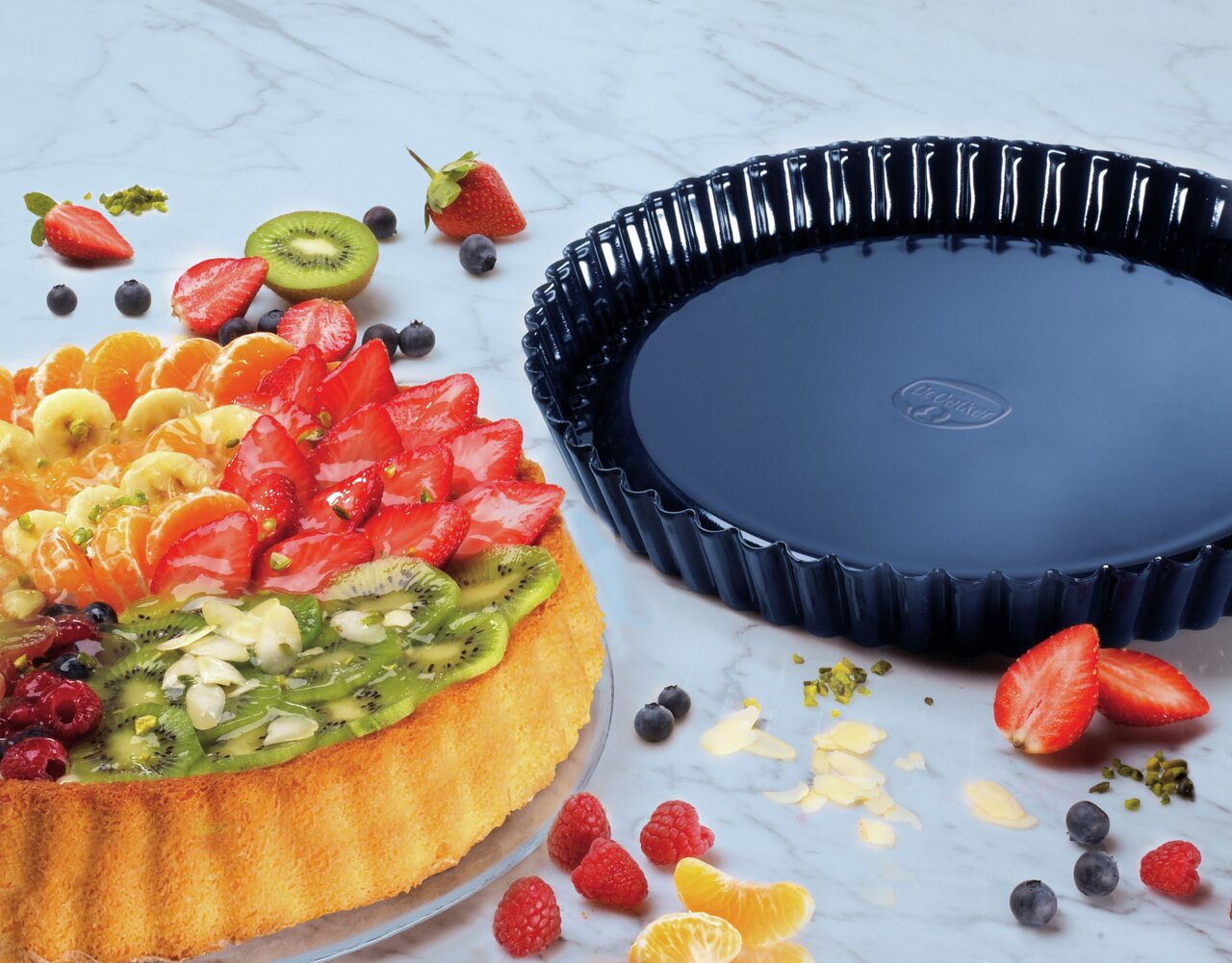 Taartvorm van 28 cm van BackLiebe, zwarte ronde bakvorm naast een versierde fruittaart, bovenaanzicht.