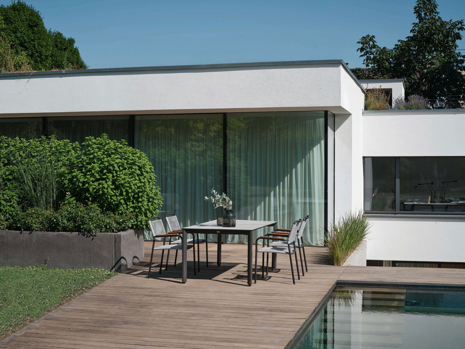 Moderner Stapelsessel auf einer Terrasse neben einem Tisch, mit Blick auf einen Garten und ein modernes Haus im Hintergrund.
