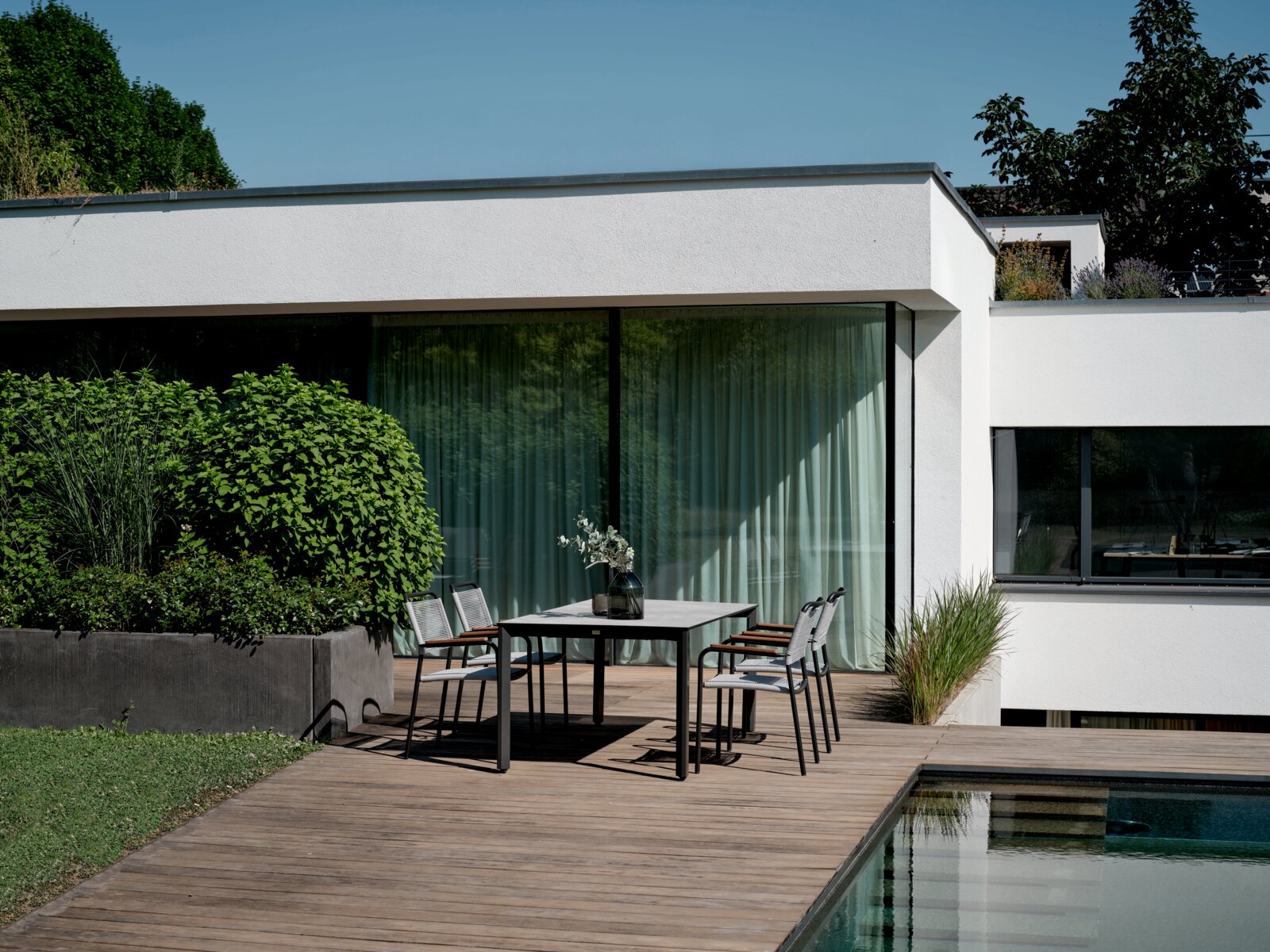 Een moderne stapelstoel op een terras naast een tafel, met uitzicht op een tuin en een modern huis op de achtergrond.