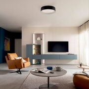 Modernes Wohnzimmer mit runder, schwarz-weißer LED-Deckenleuchte als Deckenaufbauleuchte; Ansicht von unten in leichter Untersicht, Raumaufnahme frontal.