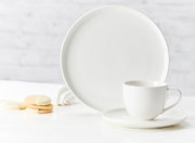 Witte koffiekop Skagen 220 ml op schotel, zijaanzicht, met bijpassend bord en koekjes op de achtergrond.