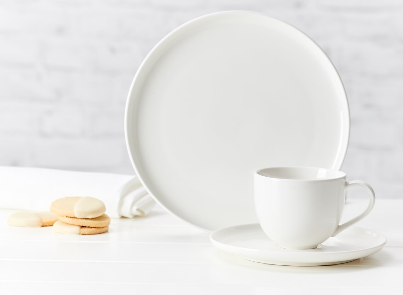 Ritzenhoff & Breker Kaffeetasse SKAGEN Weiße Kaffeetasse Skagen 220ml auf Untertasse, seitliche Perspektive, mit passendem Teller und Keksen im Hintergrund.