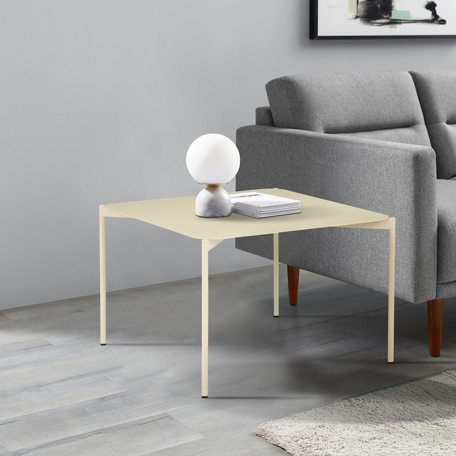 Z2 Beistelltisch JOCHEN Moderner Beistelltisch in hellem Beige, seitlich neben einem grauen Sofa platziert, mit einer dekorativen Lampe und Büchern darauf.