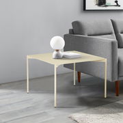 Moderner Beistelltisch in hellem Beige, seitlich neben einem grauen Sofa platziert, mit einer dekorativen Lampe und Büchern darauf.