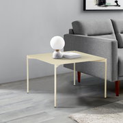 Moderner Beistelltisch in hellem Beige, seitlich neben einem grauen Sofa platziert, mit einer dekorativen Lampe und Büchern darauf.