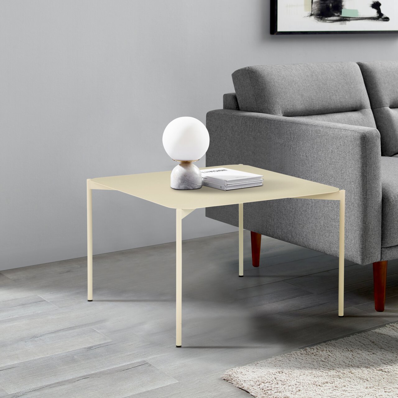 Moderner Beistelltisch in hellem Beige, seitlich neben einem grauen Sofa platziert, mit einer dekorativen Lampe und Büchern darauf.
