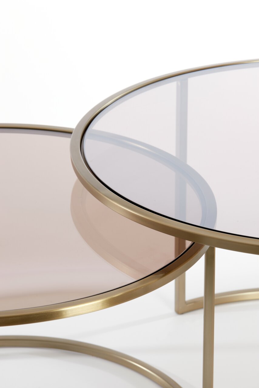 Close-up van twee ronde salontafels met een goudkleurig metalen frame en een getint glazen blad, die over elkaar zijn geschoven.