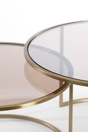 Nahaufnahme von zwei runden Couchtischen mit goldfarbenem Metallrahmen und getönter Glasplatte, übereinander geschoben.