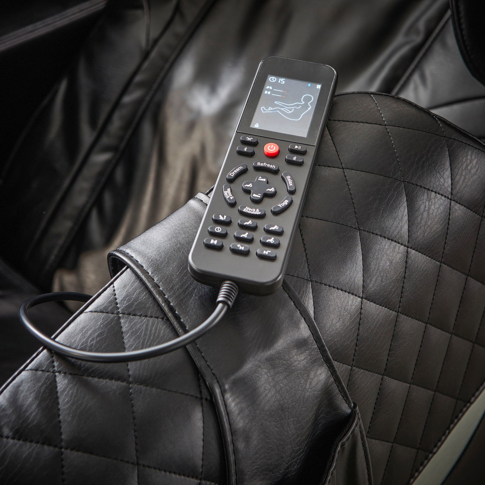 Nahaufnahme eines schwarzen Massagesessels mit einer Fernbedienung auf der Armlehne, die verschiedene Massageoptionen anzeigt.