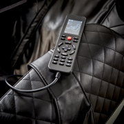 Close-up van een zwarte massagestoel met een afstandsbediening op de armleuning, waarop verschillende massageopties worden weergegeven.