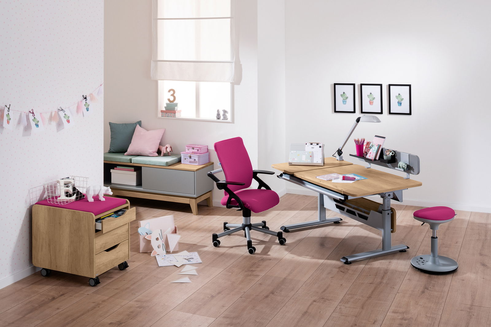 Moderner Schreibtisch mit Holzoberfläche und grauem Metallgestell, umgeben von einem pinken Drehstuhl und Hocker, in einem hellen Raum mit Holzboden, aus der Perspektive von vorne rechts betrachtet.