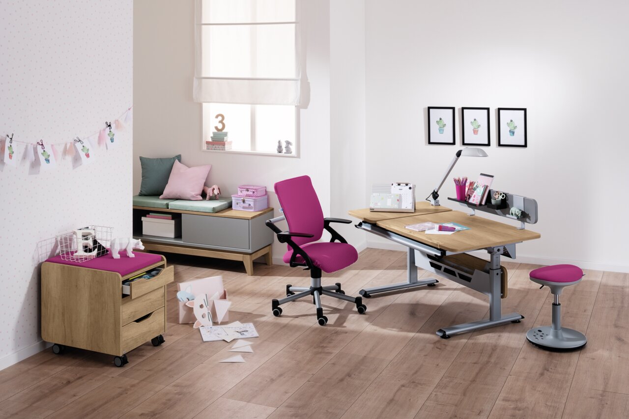 Moderner Schreibtisch mit Holzoberfläche und grauem Metallgestell, umgeben von einem pinken Drehstuhl und Hocker, in einem hellen Raum mit Holzboden, aus der Perspektive von vorne rechts betrachtet.