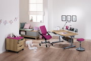 Moderner Schreibtisch mit Holzoberfläche und grauem Metallgestell, umgeben von einem pinken Drehstuhl und Hocker, in einem hellen Raum mit Holzboden, aus der Perspektive von vorne rechts betrachtet.