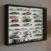 Wandmontierte Glasvitrine mit schwarzem Rahmen und mehreren Glasböden, gefüllt mit Modellautos und Sammlerstücken; Perspektive: leicht schräger Blick von vorn links