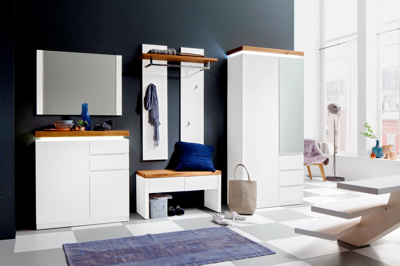 Moderne Garderobeneinrichtung in Weiß mit Holzdetails, bestehend aus einem Spiegel, einem Garderobenpaneel mit Haken, einer Bank mit Kissen und einem hohen Schrank. Perspektive von vorne.