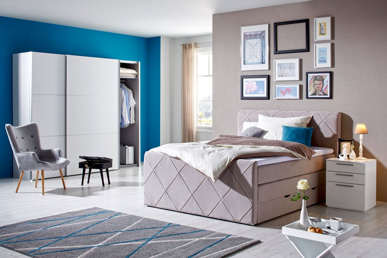 Z2 Boxspringbed SYBILLA Modernes Boxspringbett in einem stilvoll eingerichteten Schlafzimmer, seitliche Perspektive mit dekorativen Kissen und Nachttisch.