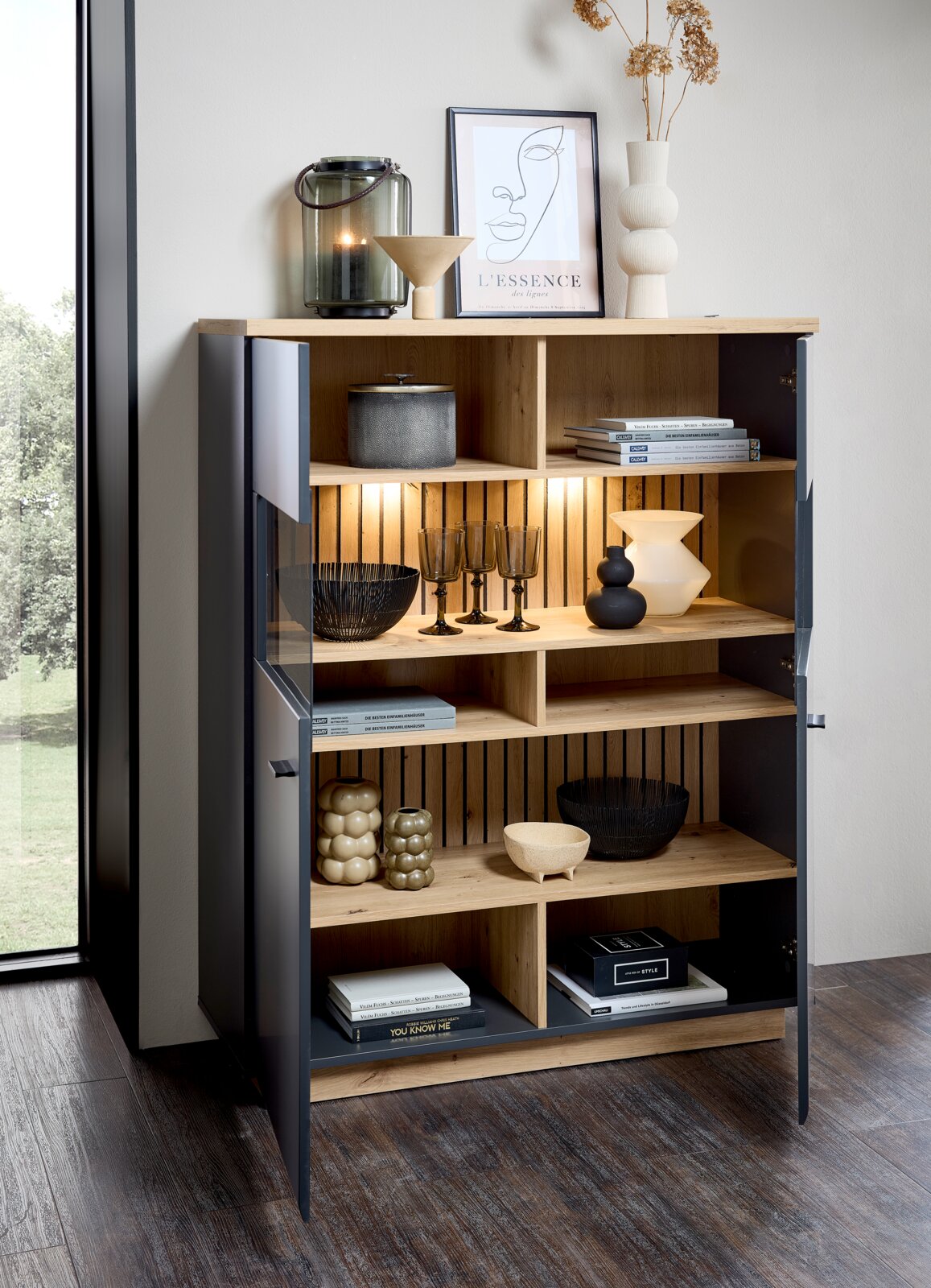 Modern hoogkastje met open en gesloten vakken, versierd met boeken, vazen en glazen, gefotografeerd vanuit een schuin perspectief.
