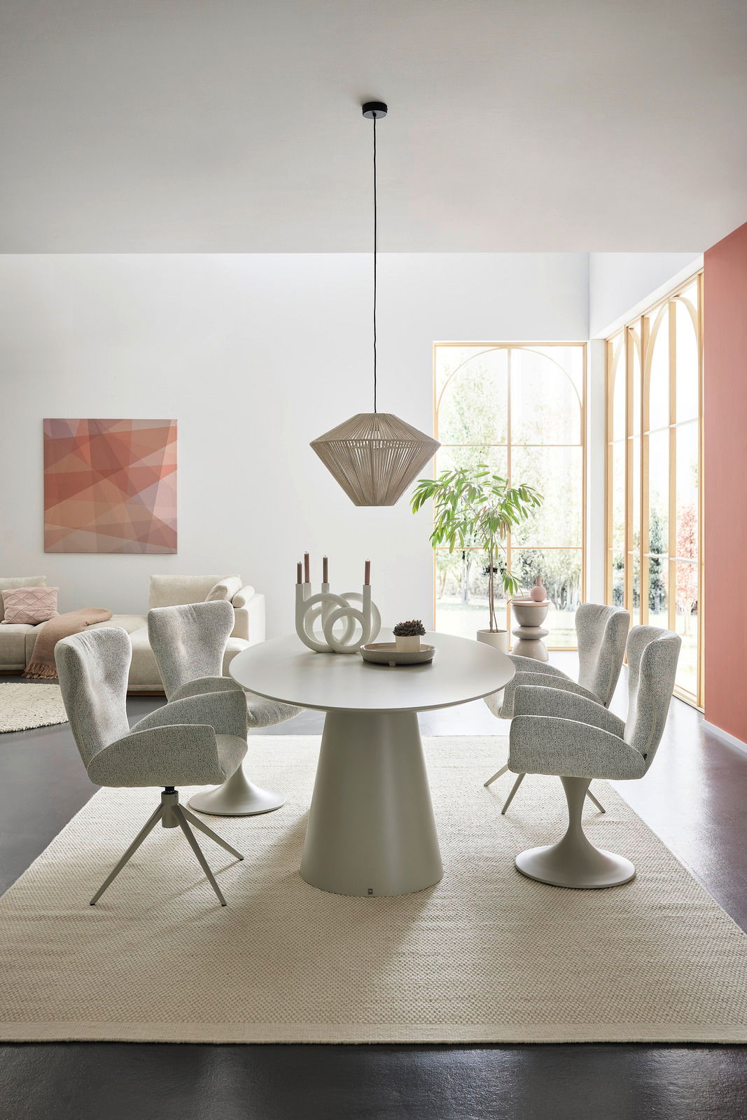 Moderner Essbereich mit rundem Esstisch und vier gepolsterten Armlehnstühlen in einem hellen Raum mit großen Fenstern, seitliche Perspektive.