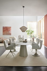 Moderner Essbereich mit rundem Esstisch und vier gepolsterten Armlehnstühlen in einem hellen Raum mit großen Fenstern, seitliche Perspektive.