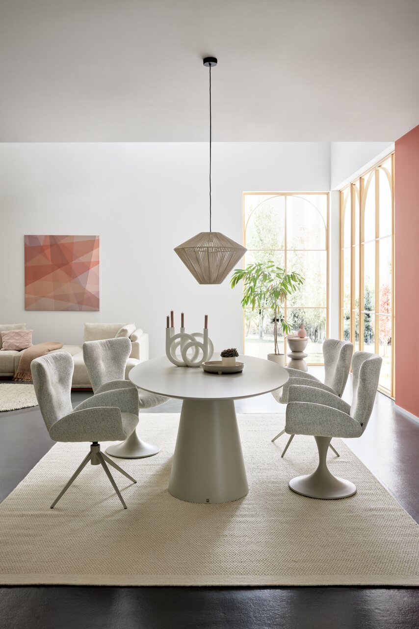 Moderner Essbereich mit rundem Esstisch und vier gepolsterten Armlehnstühlen in einem hellen Raum mit großen Fenstern, seitliche Perspektive.
