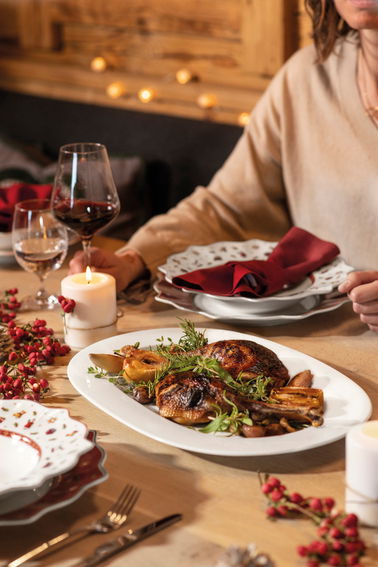 Ein festlich gedeckter Tisch mit einem Rotweinkelch im Vordergrund, begleitet von einem Teller mit gebratenem Fleisch und Beilagen. Die Perspektive zeigt eine gemütliche, einladende Atmosphäre.