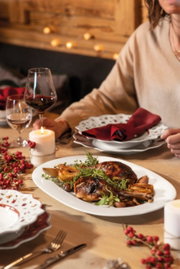 Ein festlich gedeckter Tisch mit einem Rotweinkelch im Vordergrund, begleitet von einem Teller mit gebratenem Fleisch und Beilagen. Die Perspektive zeigt eine gemütliche, einladende Atmosphäre.
