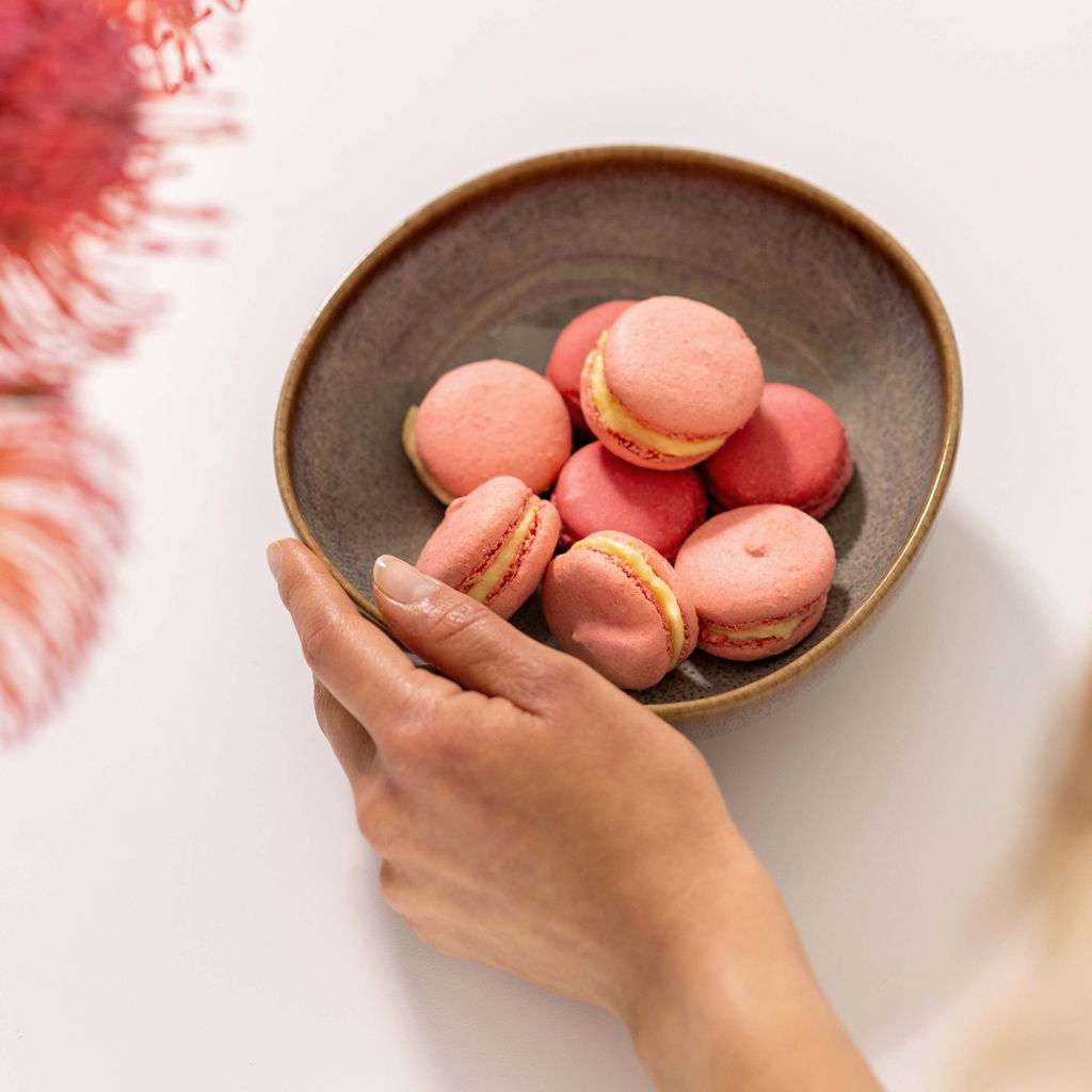 Hand hält eine beige Müslischale Lave 380ml mit rosa Macarons, von oben fotografiert.
