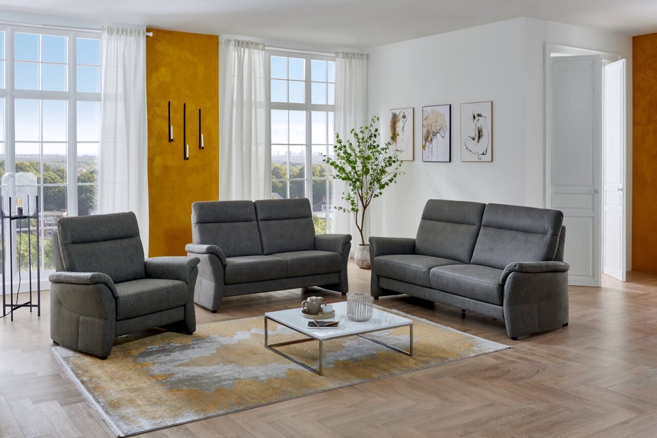 Moderne graue Polstergarnitur mit Sessel, 2-Sitzer und 3-Sitzer im hellen Wohnzimmer, frontal in leichter Schrägansicht fotografiert