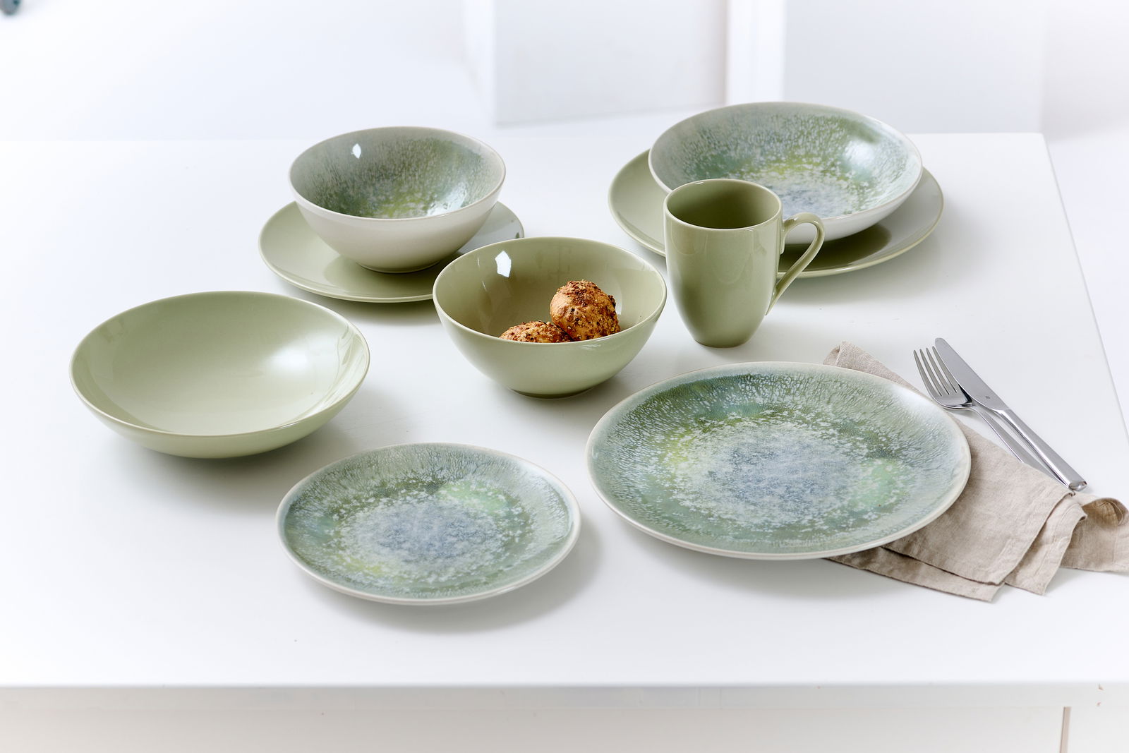 Grünes Geschirrset mit flachen und tiefen Tellern, Schalen und Tasse, von oben fotografiert.