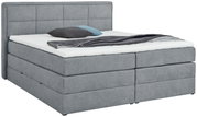 Grijs boxspringbed met hoofdeinde, gezien vanaf de zijkant, gedecoreerd met kussens en een deken.