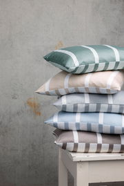 Ein Stapel von Kissenbezügen in verschiedenen Farben mit Streifenmuster, auf einem weißen Tisch vor einer grauen Wand von der Seite fotografiert.