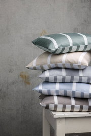 Ein Stapel von Kissenbezügen in verschiedenen Farben mit Streifenmuster, auf einem weißen Tisch vor einer grauen Wand von der Seite fotografiert.