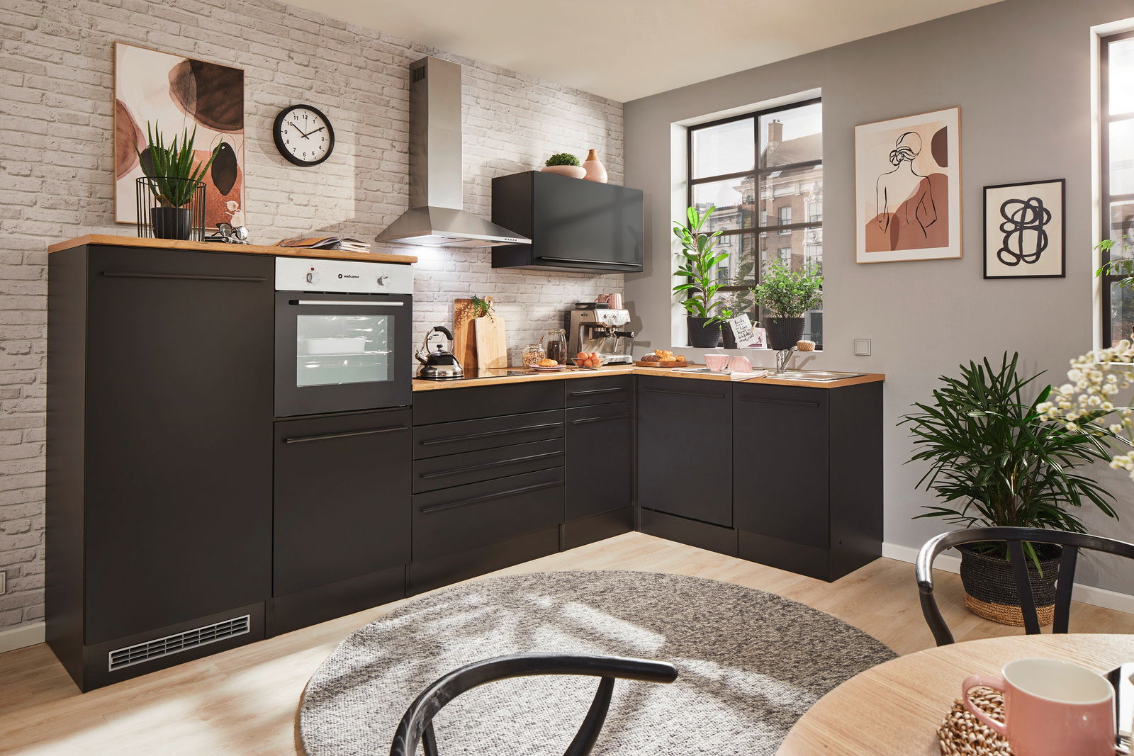 Moderne Küche mit Eckunterschrank in schwarzem Design, fotografiert aus einer leicht erhöhten Perspektive. Die Küche ist mit einem Backofen, einer Dunstabzugshaube und mehreren Pflanzen dekoriert.