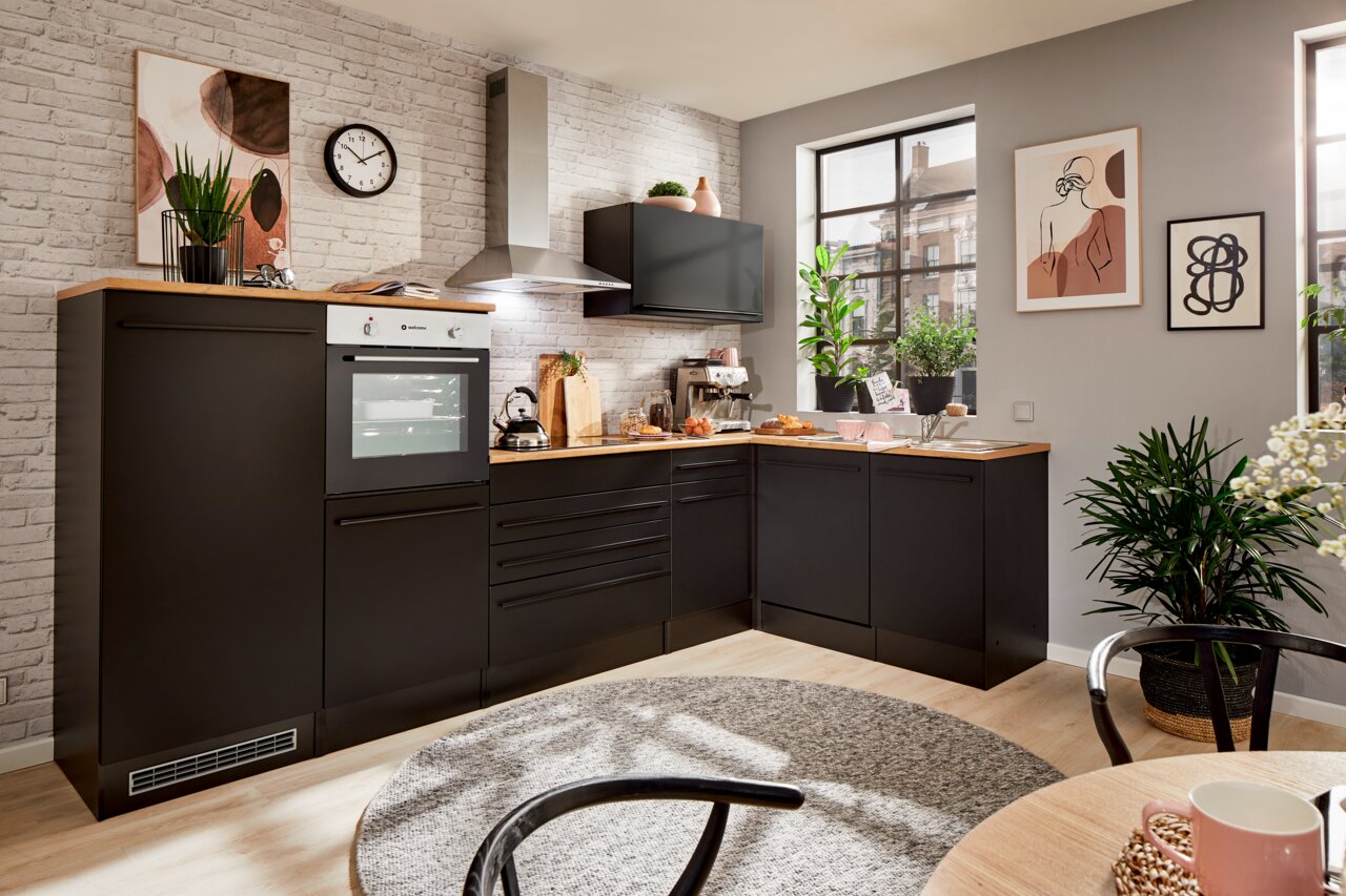 Moderne Küche mit Eckunterschrank in schwarzem Design, fotografiert aus einer leicht erhöhten Perspektive. Die Küche ist mit einem Backofen, einer Dunstabzugshaube und mehreren Pflanzen dekoriert.