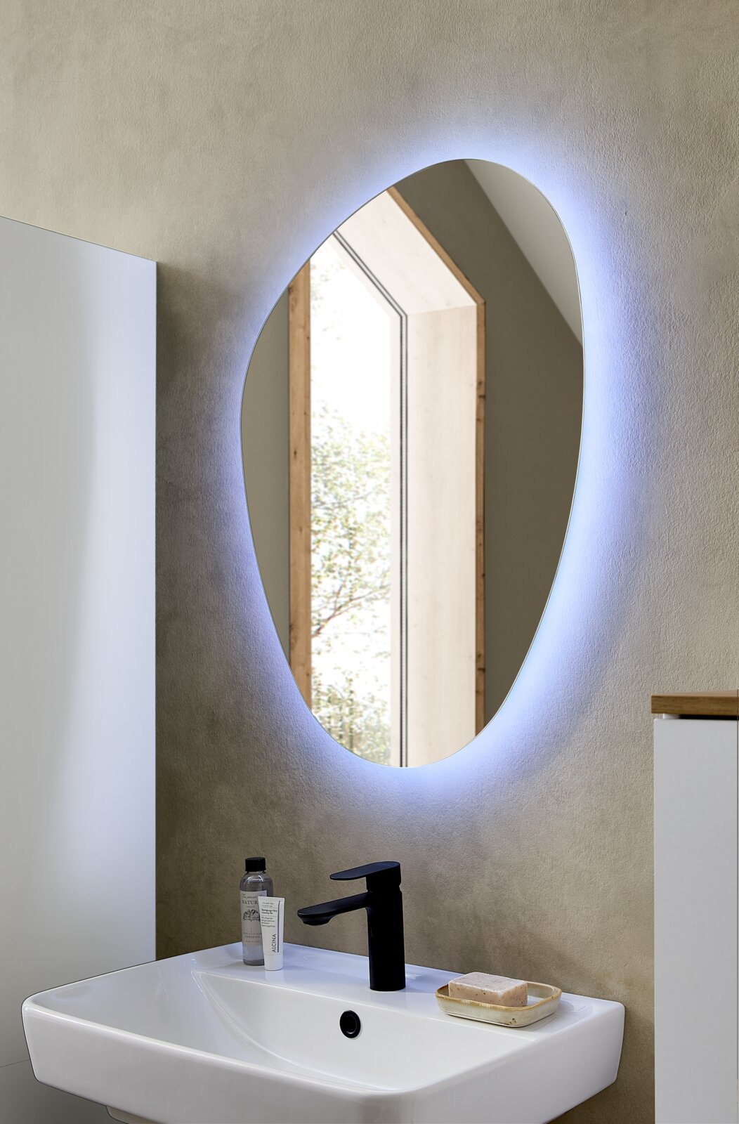 XORA Spiegel QS500 Ovaler, hinterleuchteter LED-Wandspiegel über einem weißen Waschbecken mit schwarzer Armatur im modernen Bad, frontale Ansicht leicht von links.