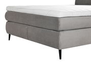 Nahaufnahme eines grauen Boxspringbetts mit gestepptem Stoffbezug und schwarzen Beinen, seitliche Perspektive