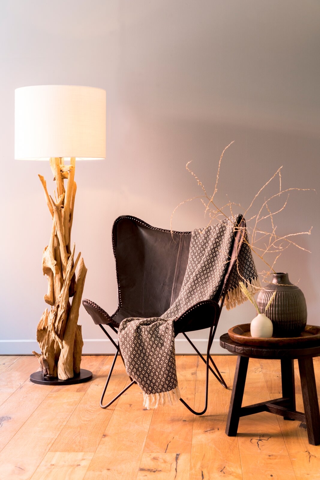 Stehleuchte mit natürlichem Holzfuß und weißem Lampenschirm, im Wohnzimmer neben einem Ledersessel und einem Beistelltisch, aus seitlicher Perspektive.