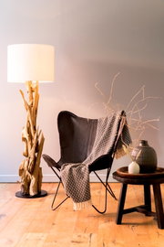 Stehleuchte mit natürlichem Holzfuß und weißem Lampenschirm, im Wohnzimmer neben einem Ledersessel und einem Beistelltisch, aus seitlicher Perspektive.