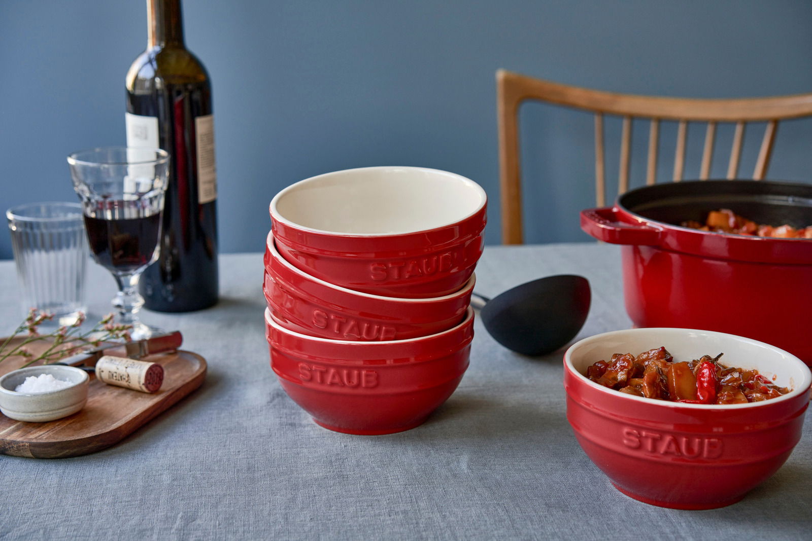 Ein Set aus vier kirschroten Schüsseln, gestapelt auf einem Tisch, mit einer gefüllten Schüssel im Vordergrund. Perspektive von der Seite.